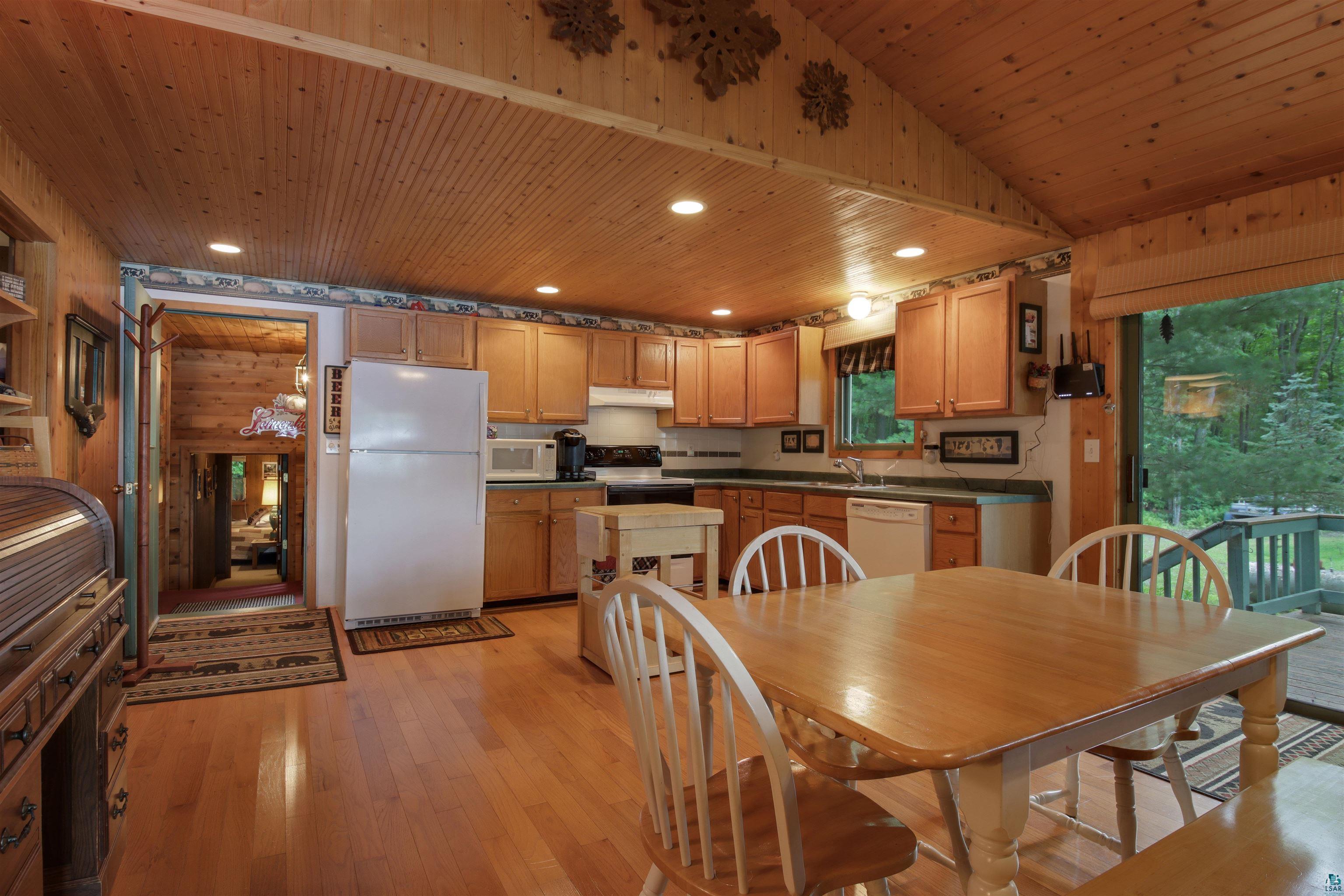 N5063 First Street Spooner, WI 54801 - Photo 14 of 36 Kitchen with wooden walls, light brown cabinets, white appliances, light hardwood / wood-style floors, and wooden ceiling
