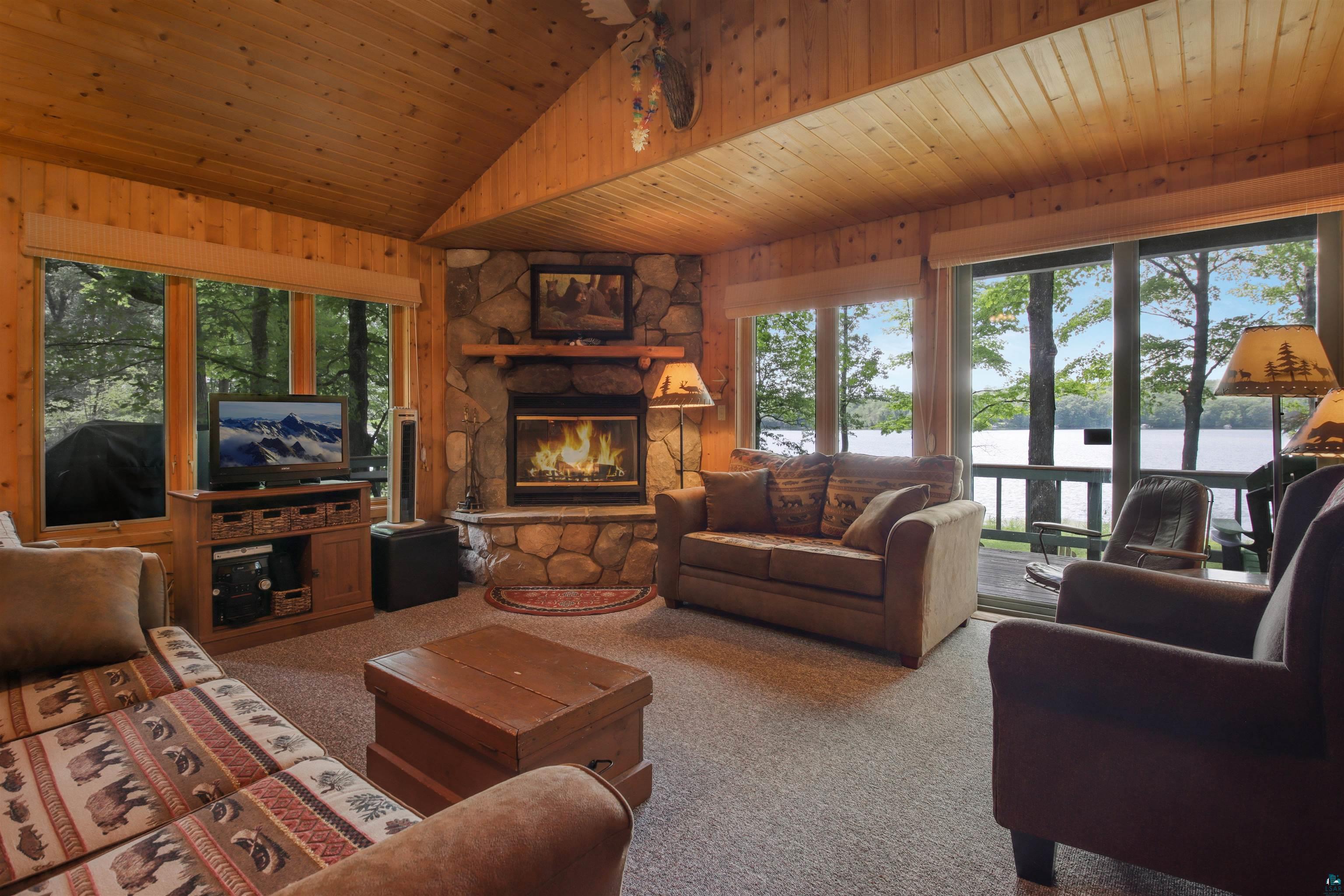 N5063 First Street Spooner, WI 54801 - Photo 21 of 36 Living room with a fireplace, a water view, wooden ceiling, light colored carpet, and vaulted ceiling