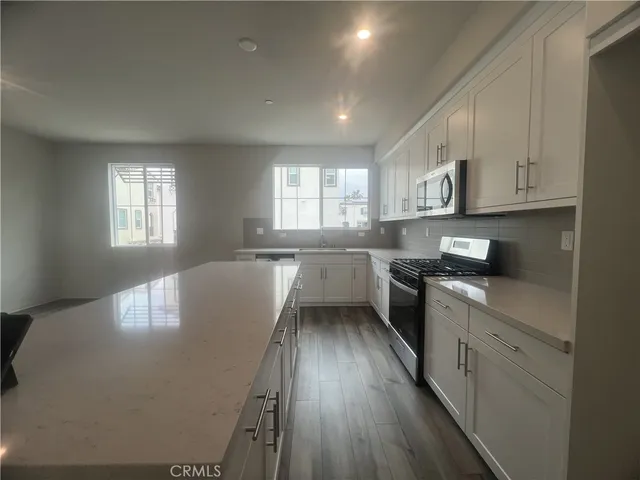 a kitchen with stainless steel appliances granite countertop a refrigerator a sink dishwasher a stove and white countertops with wooden floor