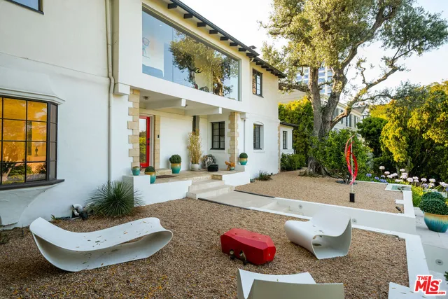 a view of a white house with couches potted plants and a fountain