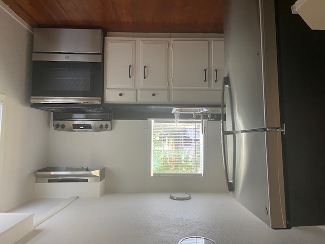 417 South Commerce Street, Unit B Lockhart, TX 78644 - Photo 4 of 9 Kitchen with stainless steel appliances, a textured ceiling, extractor fan, white cabinetry, and dark wood finished floors