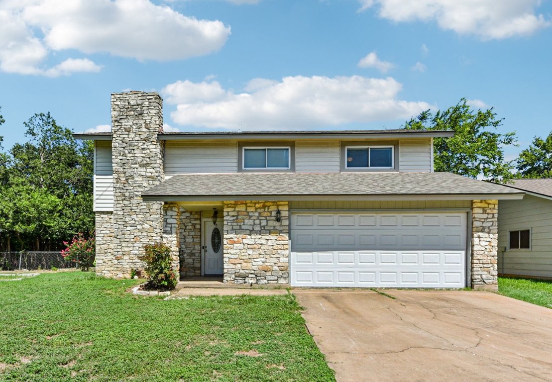 View of front facade with driveway, stone siding, a chimney, an attached garage, and a shingled roof