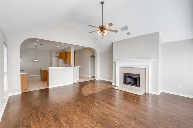 a view of a room with a kitchen a fireplace a ceiling fan and wooden floor