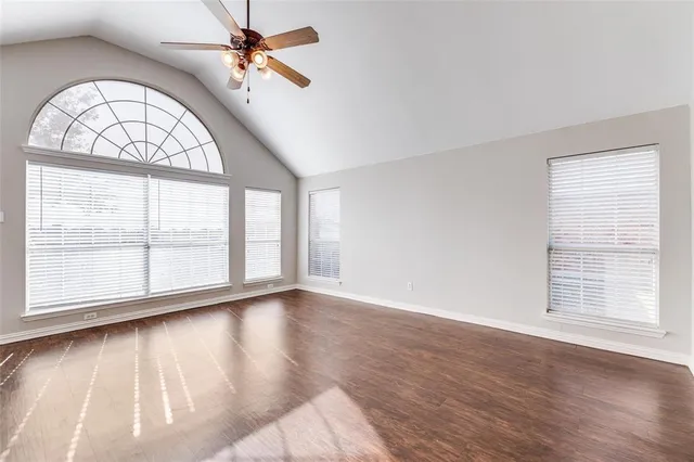 an empty room with wooden floor chandelier fan and windows