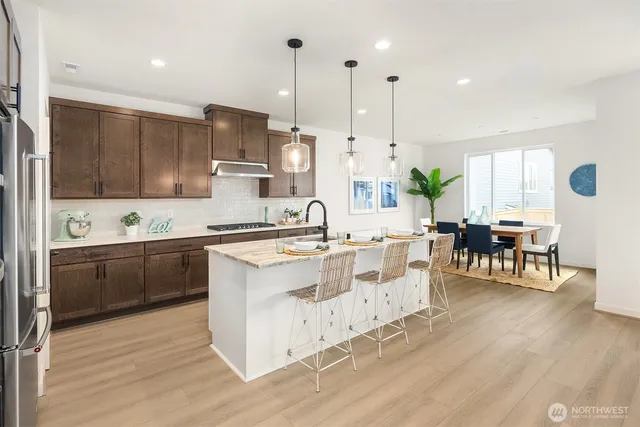 a large kitchen with kitchen island granite countertop a stove a sink a refrigerator and white cabinets with wooden floor