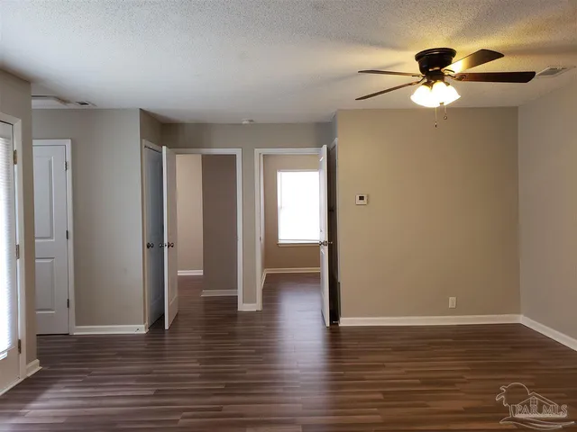 a view of an empty room with wooden floor and a ceiling fan