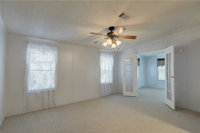 an empty room with chandelier fan and windows
