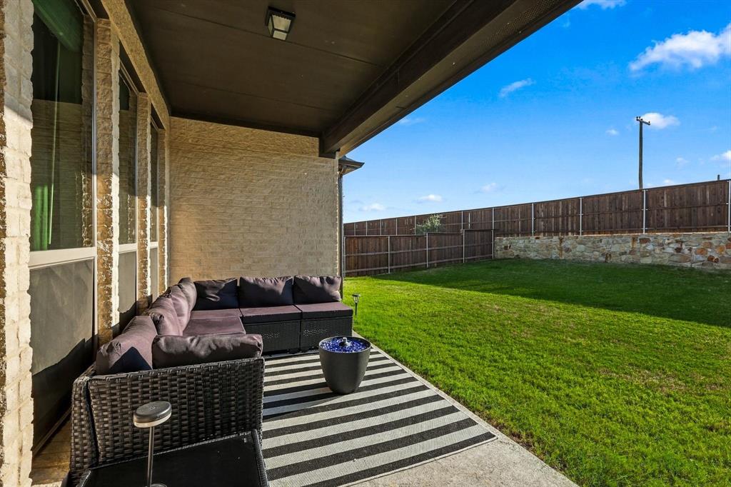 137 Chisos Court Rhome, TX 76078 - Photo 38 of 40 Covered patio with concrete flooring, stone veneer exterior, a spacious lawn area, and a wood privacy fence on a stone base