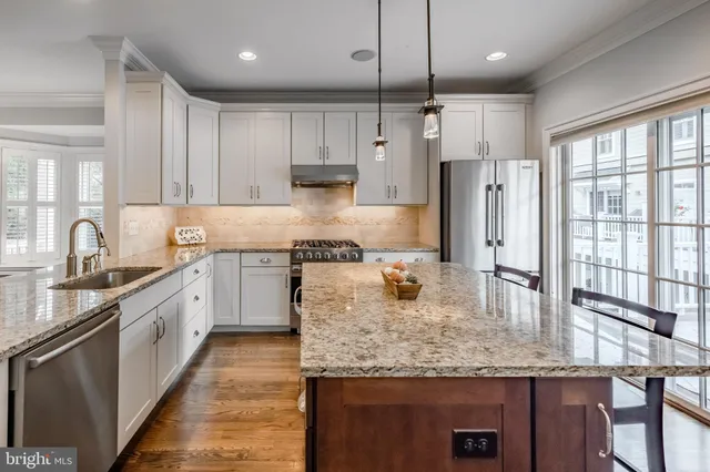 a kitchen with kitchen island granite countertop a stove a sink a center island and a wooden floor