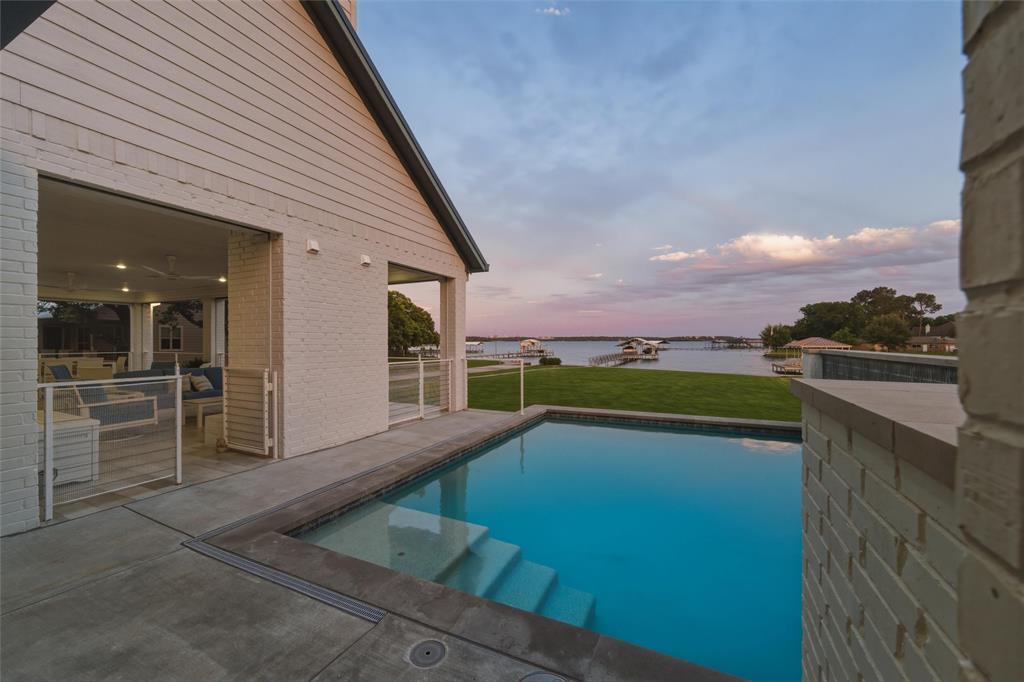 6625 Sandy Beach Road Azle, TX 76020 - Photo 29 of 40 Pool area features in-ground rectangular pool with integrated entry steps, surrounding deck space, painted brick privacy walls, and open waterfront views extending across the rear lawn area. Covered patio spaces connect directly to the pool and outdoor living areas.