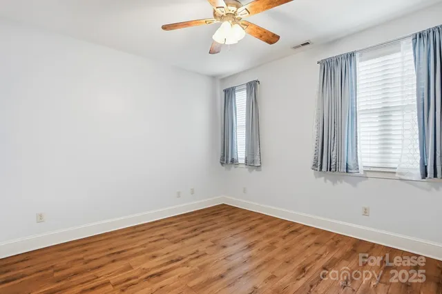an empty room with wooden floor fan and windows