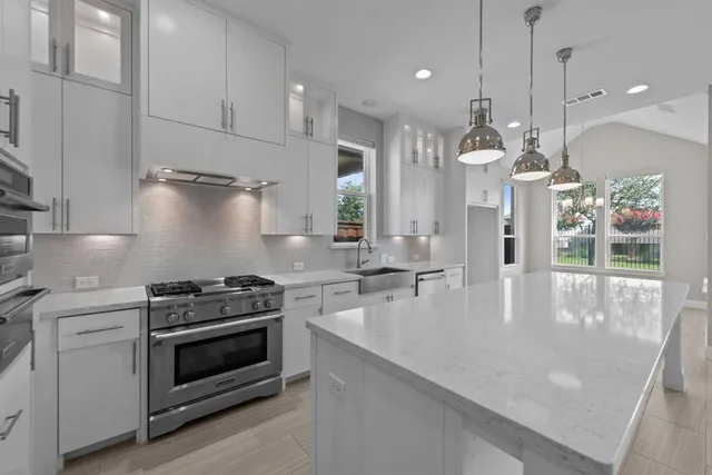 a kitchen with stainless steel appliances kitchen island granite countertop a sink a stove a refrigerator and white cabinets