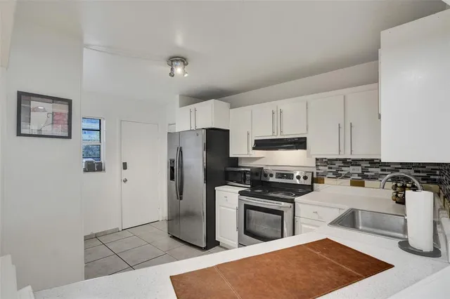 a kitchen with stainless steel appliances granite countertop a stove top oven a sink a refrigerator and white cabinets