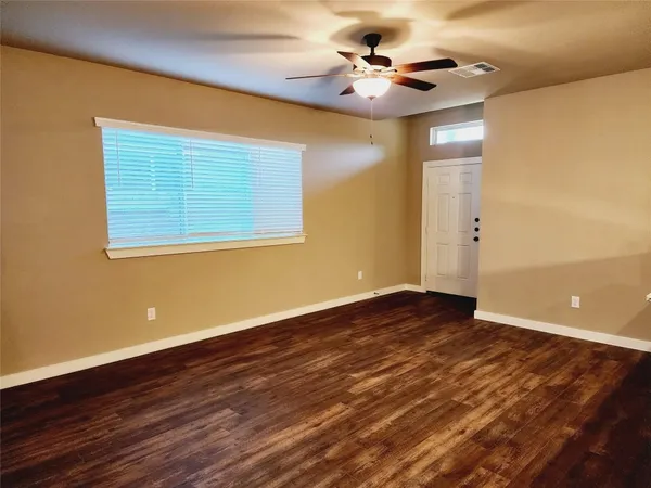 a view of an empty room with wooden floor and a ceiling fan