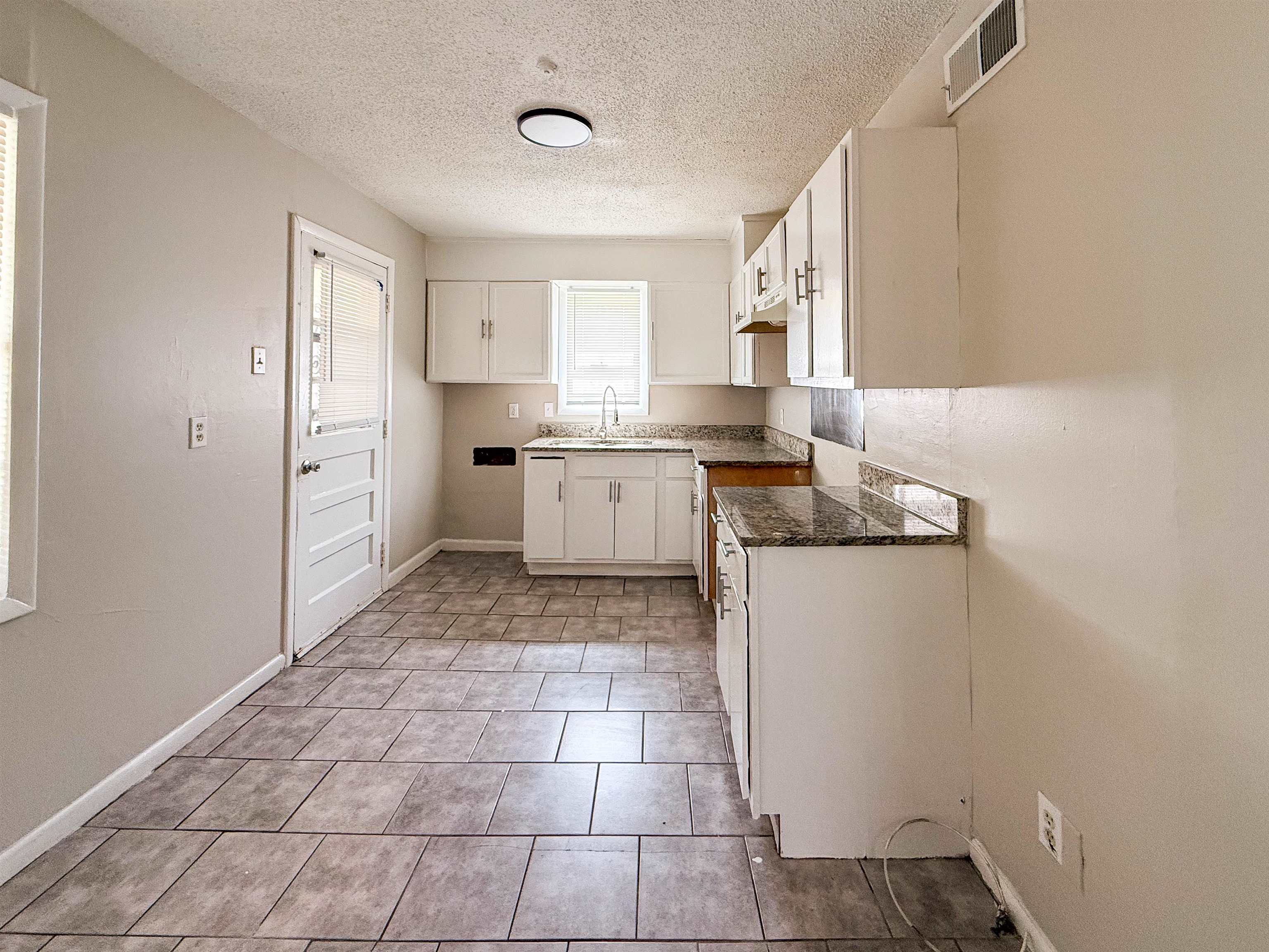 655 West Raines Road Memphis, TN 38109 - Photo 7 of 18 Kitchen featuring a textured ceiling, white cabinets, dark stone countertops, and light tile patterned floors