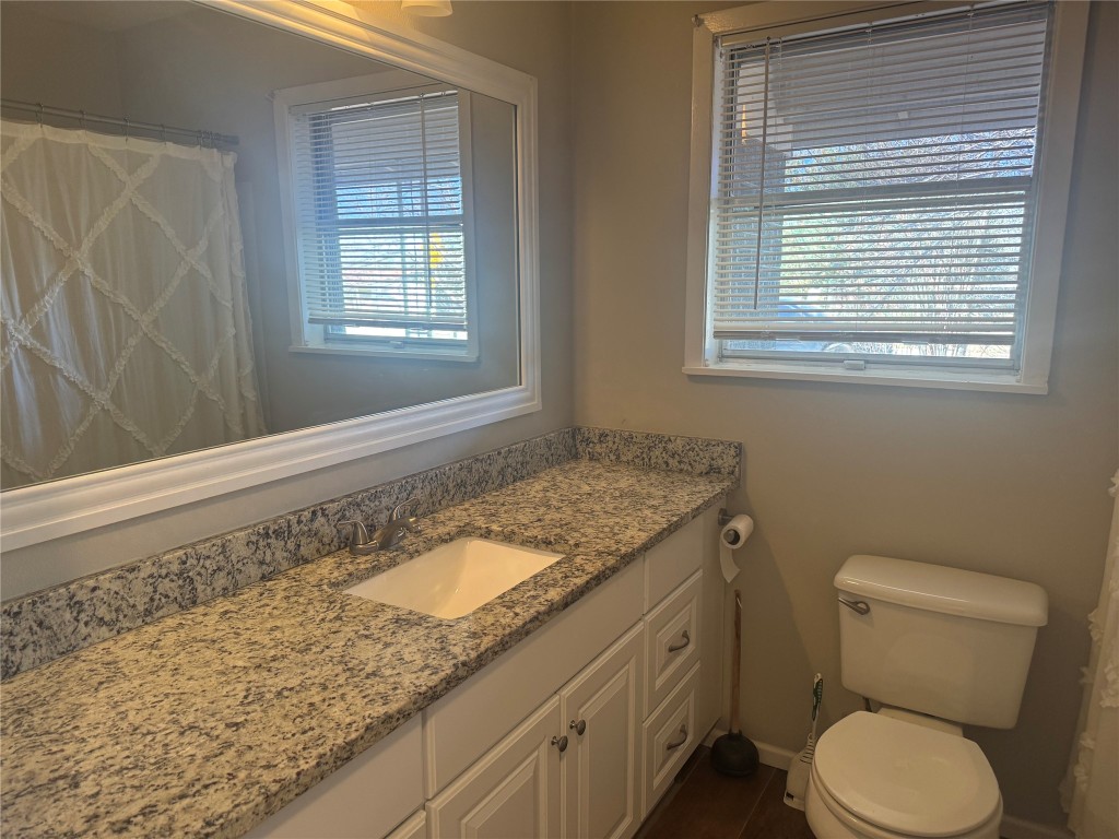 6007 Libyan Drive Austin, TX 78745 - Photo 6 of 8 a bathroom with a granite countertop toilet a sink a mirror and a window