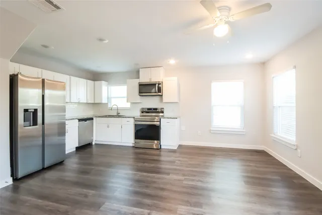 a kitchen with granite countertop a refrigerator oven a sink dishwasher and white cabinets with wooden floor