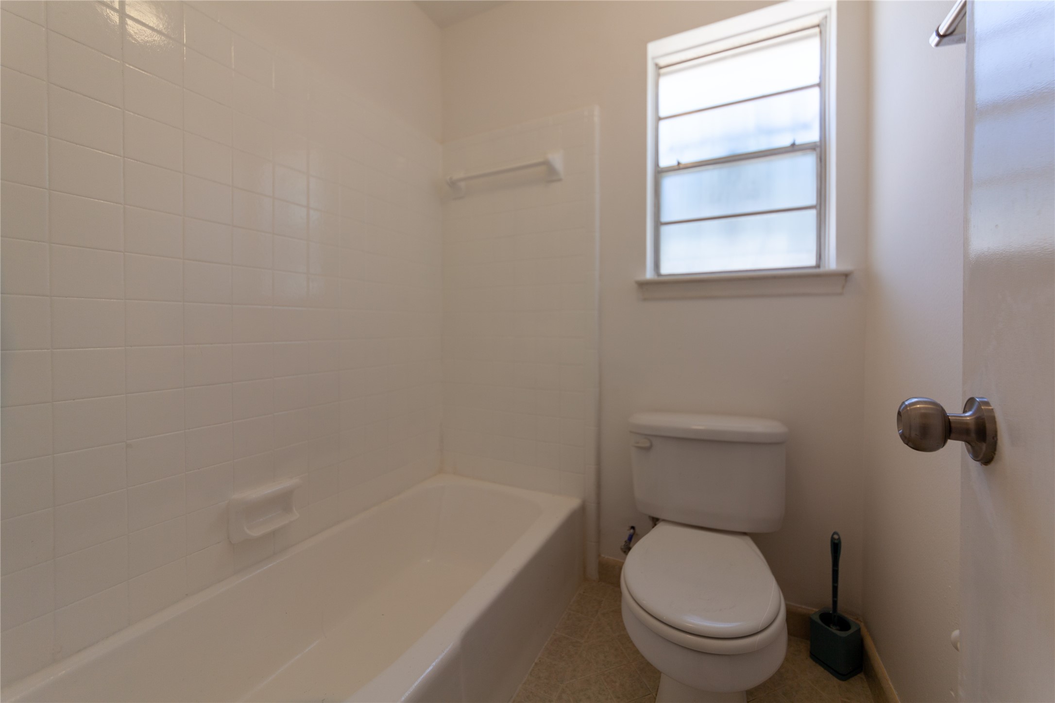 8826 Roos Road Houston, TX 77036 - Photo 17 of 42 This primary bathroom features a simple design with a white tiled bathtub, standard toilet, and a window providing natural light.
