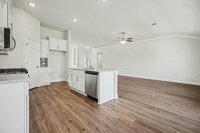 a large white kitchen with kitchen island a sink a stove a refrigerator and white cabinets with wooden floor