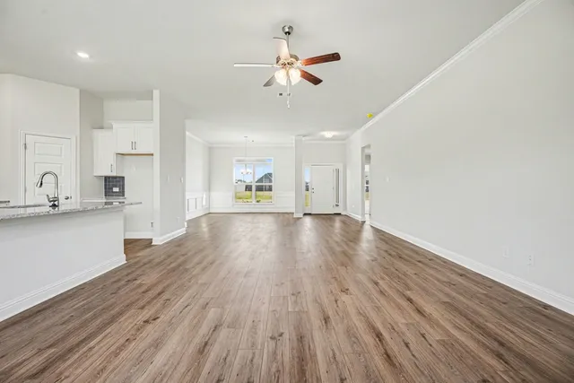 a view of an empty room and kitchen view with wooden floor