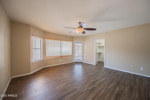 a view of an empty room with wooden floor and a ceiling fan
