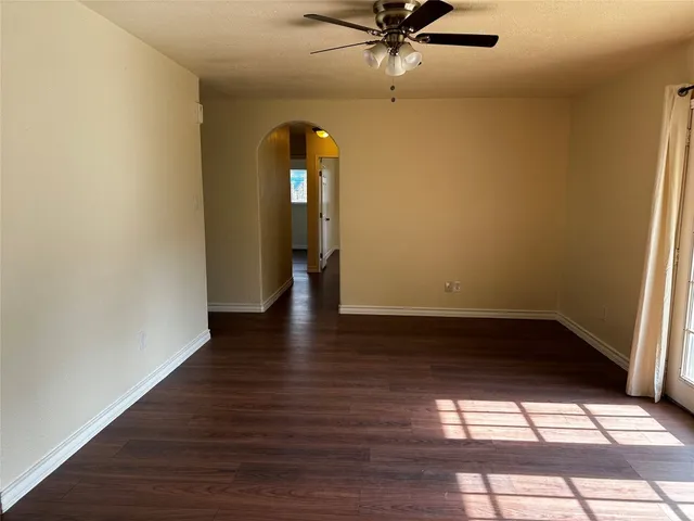 an empty room with wooden floor fan and windows