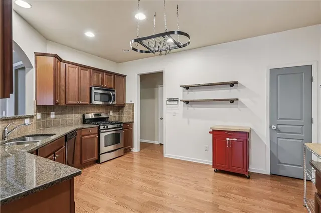 a kitchen with stainless steel appliances granite countertop a refrigerator a stove top oven a sink dishwasher and wooden cabinets with wooden floor