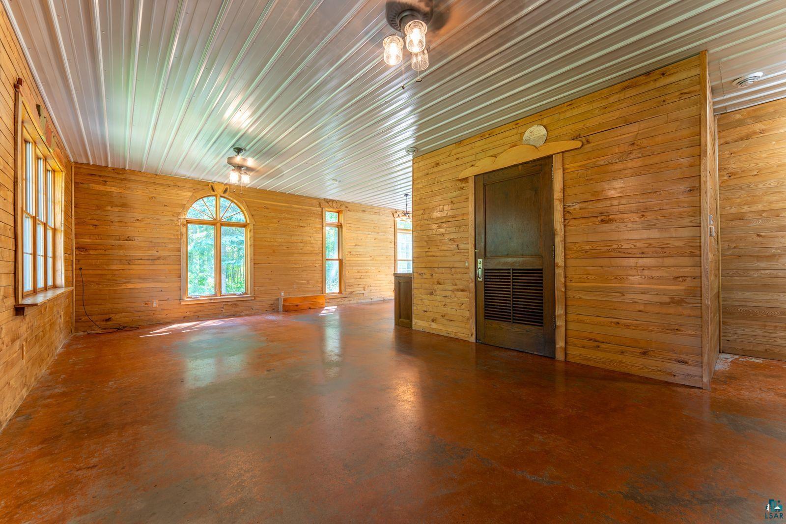 9734 Alango Road Angora, MN 55703 - Photo 4 of 41 Expansive room featuring horizontal wood-panel walls, a corrugated metal ceiling, and a polished concrete floor