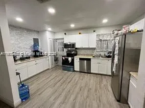 a kitchen with stainless steel appliances granite countertop a stove top oven a sink dishwasher a refrigerator and white cabinets with wooden floor