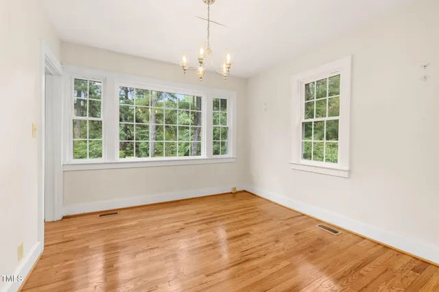 an empty room with chandelier fan and windows