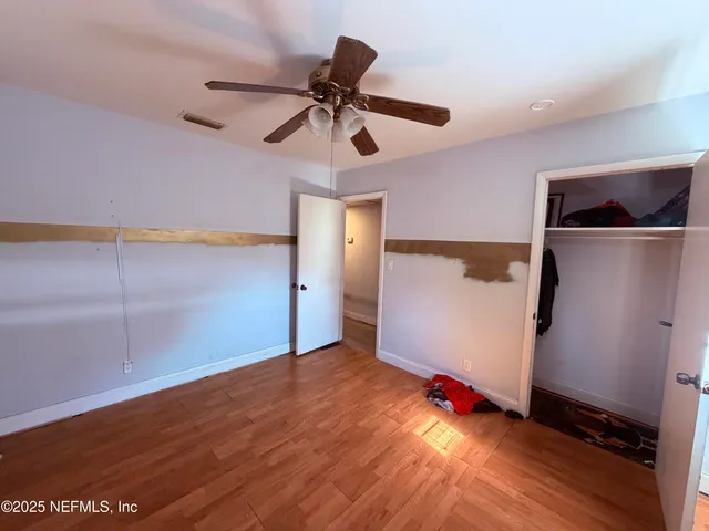 an empty room with wooden floor closet fan and windows