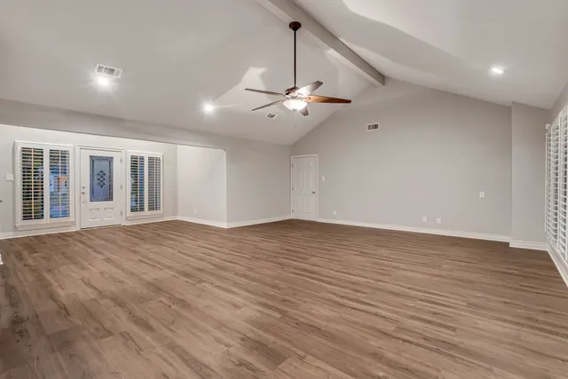 a view of an empty room with wooden floor and a ceiling fan