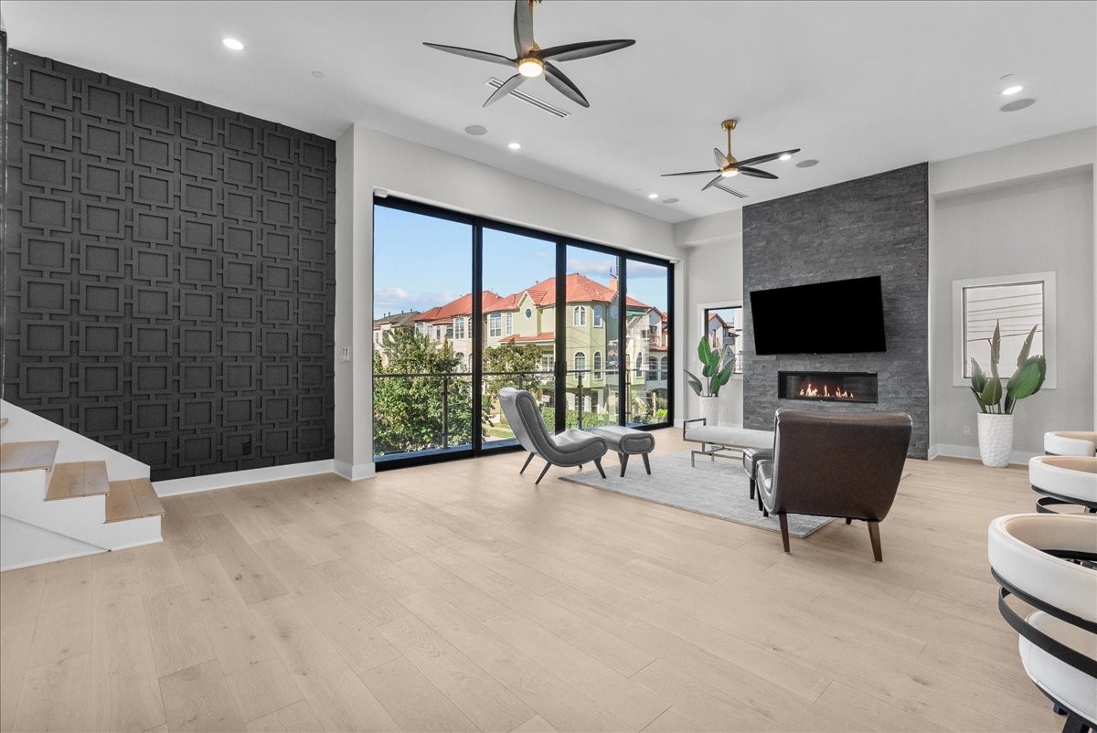 516 Reinerman Street Houston, TX 77007 - Photo 21 of 42 This modern living room features large floor-to-ceiling windows with a scenic view, a sleek fireplace, and stylish furnishings. The space is bright with light wood flooring, a textured accent wall, and ceiling fans, offering a blend of comfort and elegance.