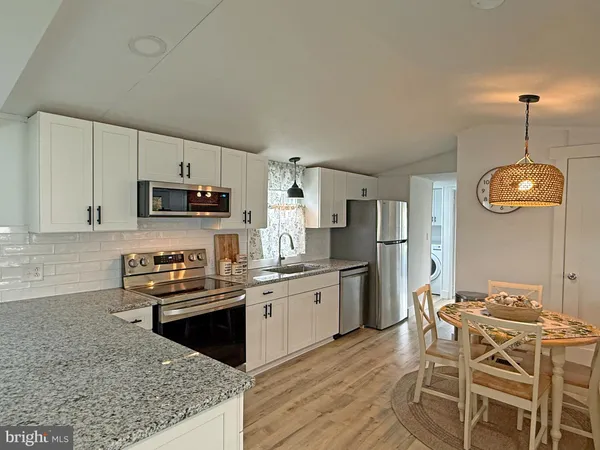 a kitchen with stainless steel appliances granite countertop a stove top oven a refrigerator a sink dishwasher a dining table and chairs with wooden floor