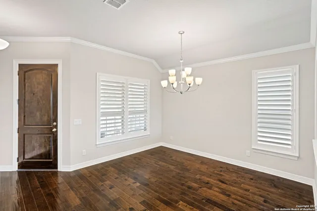 an empty room with wooden floor chandelier and windows