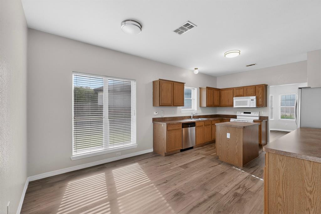 3401 Newgate Street Midlothian, TX 76065 - Photo 12 of 34 Kitchen featuring wood-finish flooring, wood cabinetry, a center island, stainless steel dishwasher, and a window with blinds