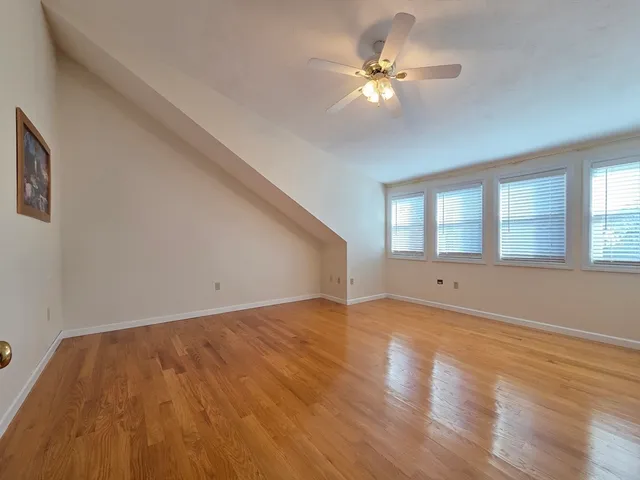 a view of an empty room with chandelier fan and wooden floor