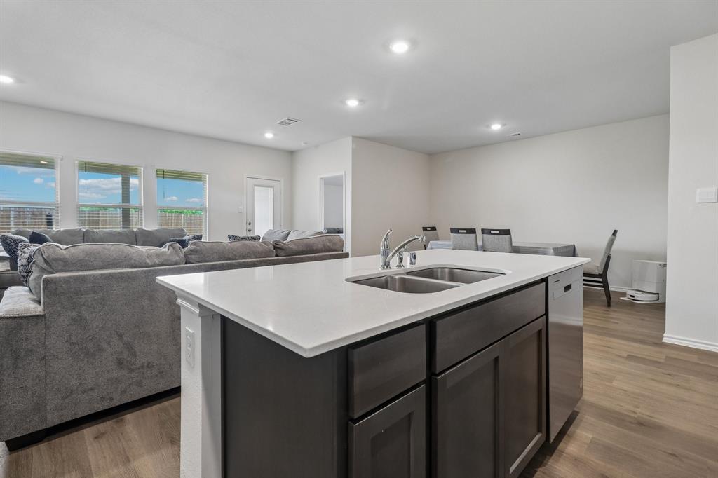 1453 Millstead Rill Road Caddo Mills, TX 75135 - Photo 8 of 40 Kitchen island featuring a dual-basin stainless steel sink, a chrome faucet, dark wood-finish cabinetry, and a light-toned countertop