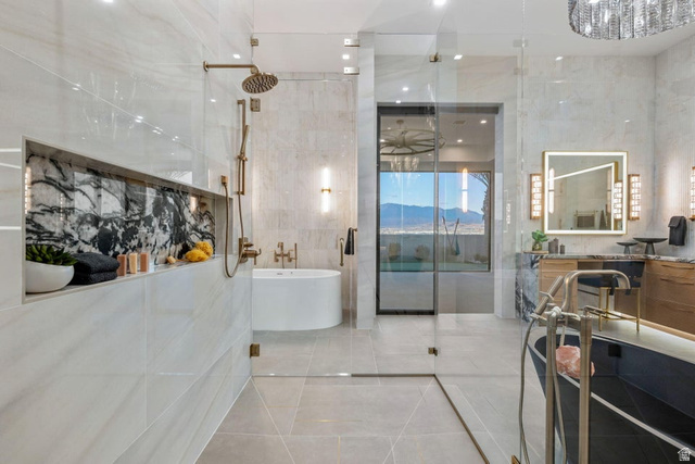 2867 East Granite Way St. George, UT 84790 - Photo 29 of 69 Contemporary bathroom featuring a spacious glass-enclosed shower with bronze fixtures, a built-in shelf with dark veined stone accent, a freestanding soaking tub, a dual vanity with illuminated mirror, and large format tile flooring