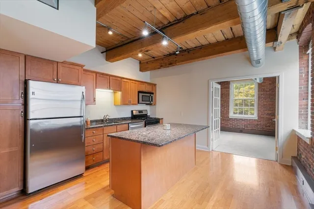 a kitchen with stainless steel appliances granite countertop a refrigerator a sink dishwasher a stove and a dining table with wooden floor