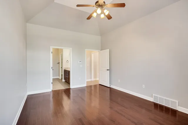 a view of an empty room with wooden floor and a ceiling fan