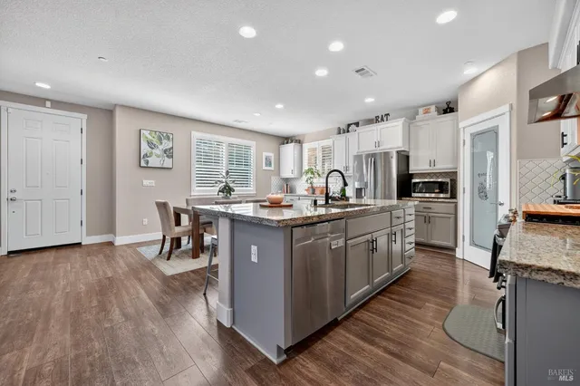 a kitchen with stainless steel appliances granite countertop a refrigerator a stove top oven a sink dishwasher and white cabinets with wooden floor