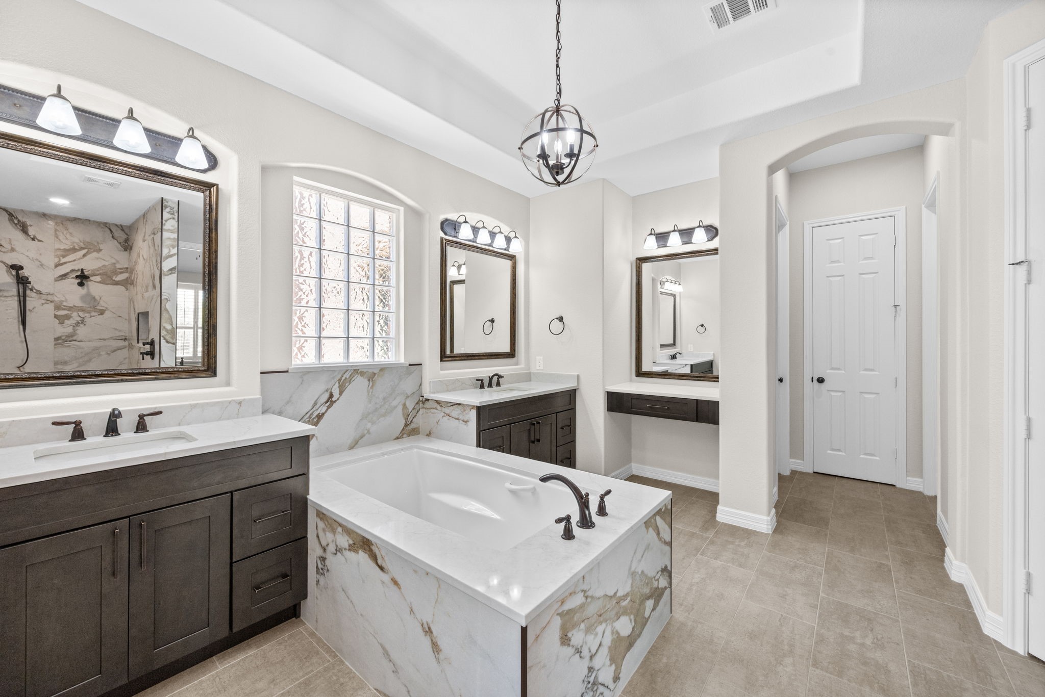 27642 Linden Ridge Lane Fulshear, TX 77441 - Photo 20 of 42 The relaxing soaking tub is nestled beneath a privacy-block window and surrounded by elegant Quartz, creating a luxurious spa-like retreat. Nearby, a dedicated makeup vanity provides the perfect space to get ready each day. In the distance, doors lead to two separate walk-in closets and a convenient linen closet, offering exceptional storage and organization.