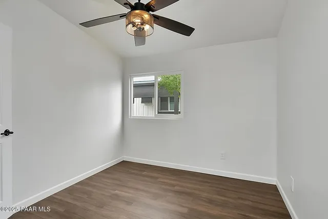 an empty room with wooden floor chandelier fan and windows