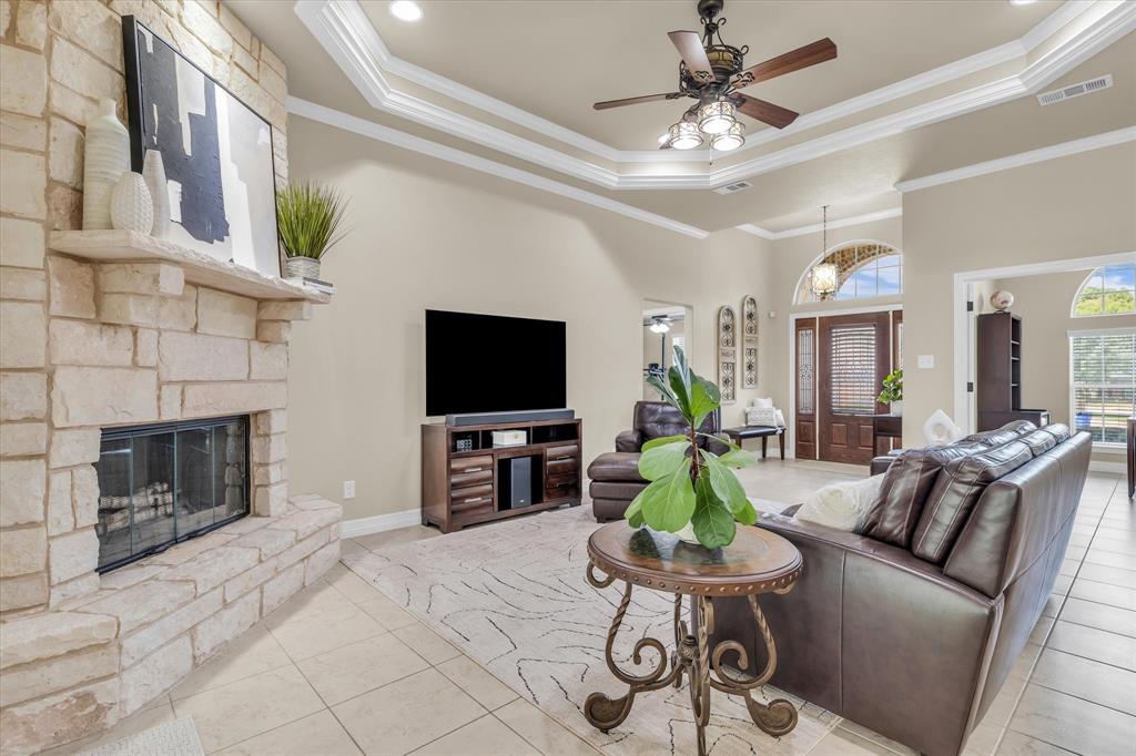 910 Springdale Lane Lorena, TX 76655 - Photo 7 of 39 Living area featuring a stone fireplace with hearth, tile flooring, tray ceiling with crown molding, and a ceiling fan