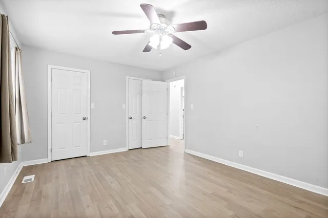 an empty room with wooden floor ceiling fan and window