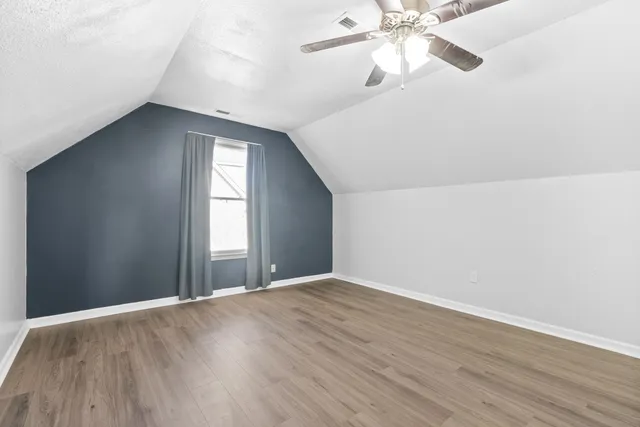 a view of an empty room with wooden floor and a ceiling fan