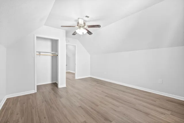an empty room with wooden floor fan and windows
