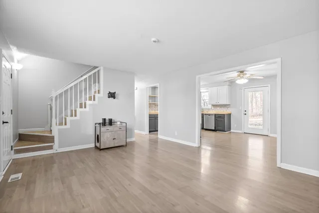 a view of an empty room and a kitchen with wooden floor windows