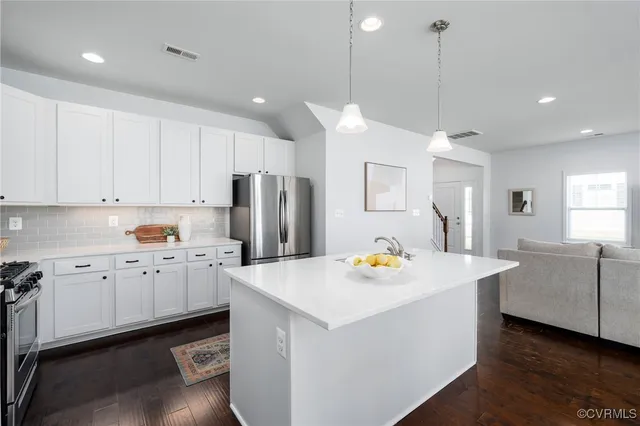 a kitchen with stainless steel appliances kitchen island granite countertop a refrigerator a sink dishwasher a stove and white cabinets with wooden floor